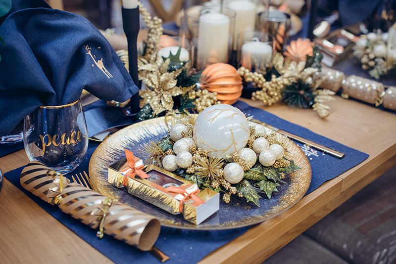 Christmastime table setting, festive dinnerware decorated with details and white balls in Blue and Gold colors. Navy Blue Table Linens and Gold Cutlery. Trends of Winter Holiday Tablescape Decor